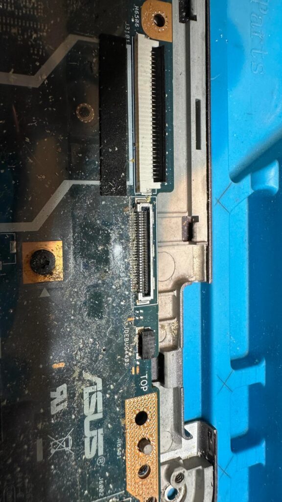 Uma imagem aproximada de uma placa-mãe ASUS mostrando conectores e trilhas expostos, com o texto 'TOP' visível.