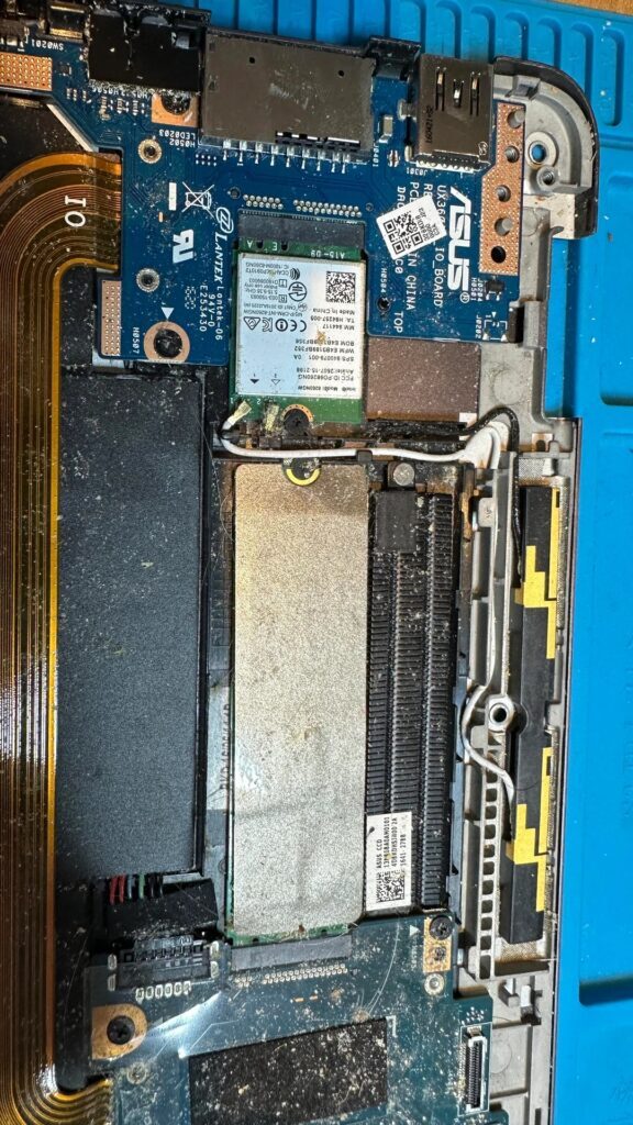 A imagem mostra os componentes internos de um laptop ASUS, incluindo uma placa Wi-Fi e um módulo de RAM, instalados em uma placa-mãe empoeirada identificada como 'X401A MAIN BOARD REV 2.3'.