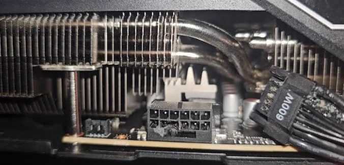 Uma imagem aproximada de uma placa de vídeo mostrando um conector de alimentação de 12 pinos descoberto e um cabo de alimentação identificado como '600W' ao lado do dissipador de calor.