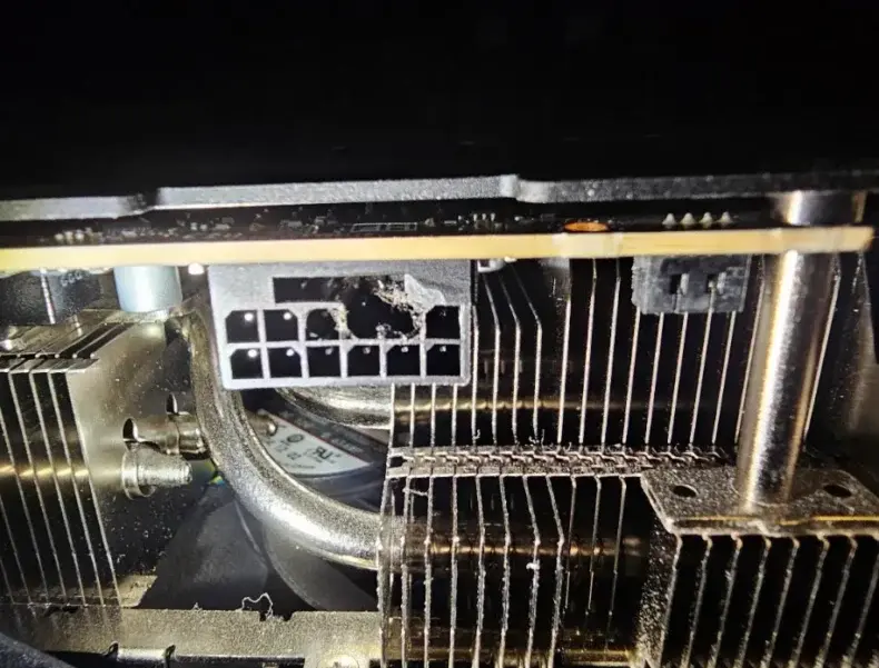 Um conector de alimentação danificado está visível em uma placa de vídeo, cercado por aletas metálicas do dissipador de calor.